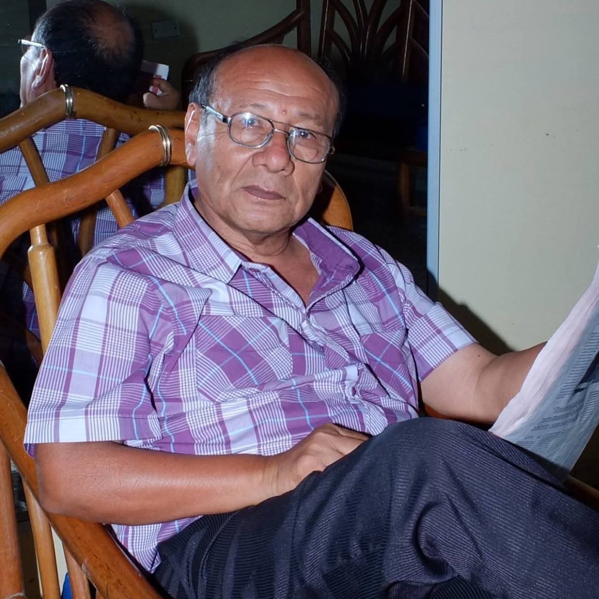 Mario Sabogal sentado en un sillón de mimbre, leyendo